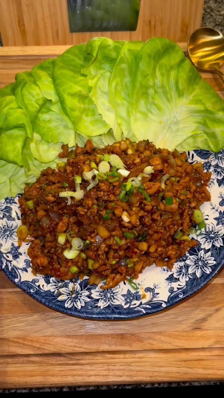 Minced chicken filling with green onions and fresh butter lettuce leaves on a plate.