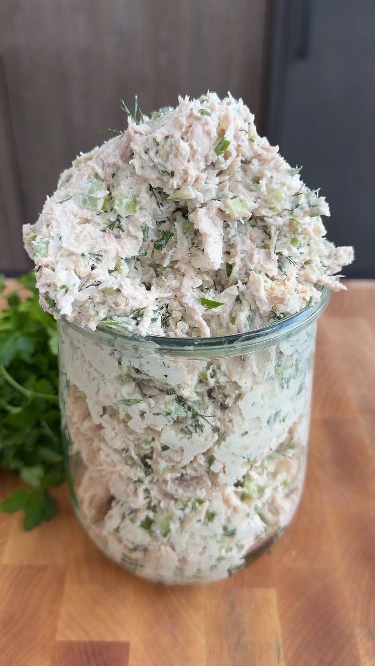 Creamy chicken salad with green vegetables piled in a glass jar on wood.