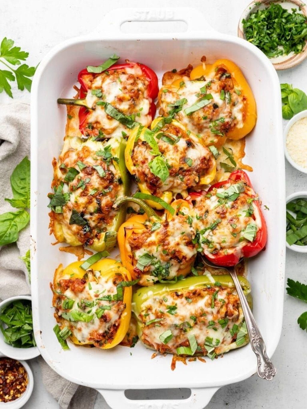 Stuffed bell peppers with melted cheese and herbs in a white baking dish.