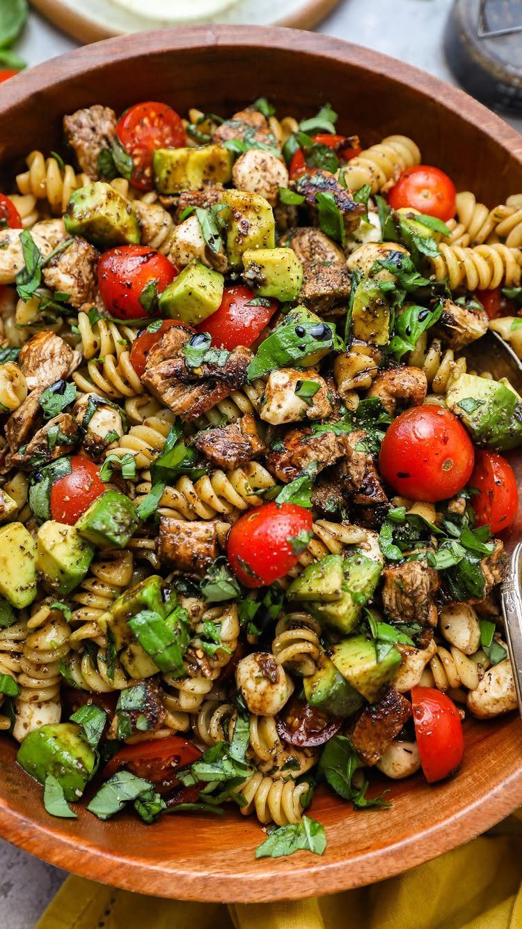 Rotini pasta salad with grilled chicken, cherry tomatoes, zucchini, and fresh basil leaves.