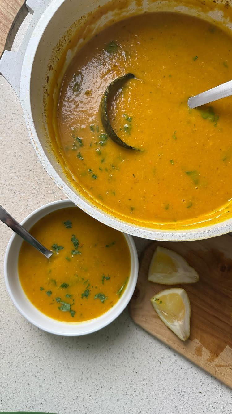Orange lentil soup in a white pot and bowl with lemon wedges.