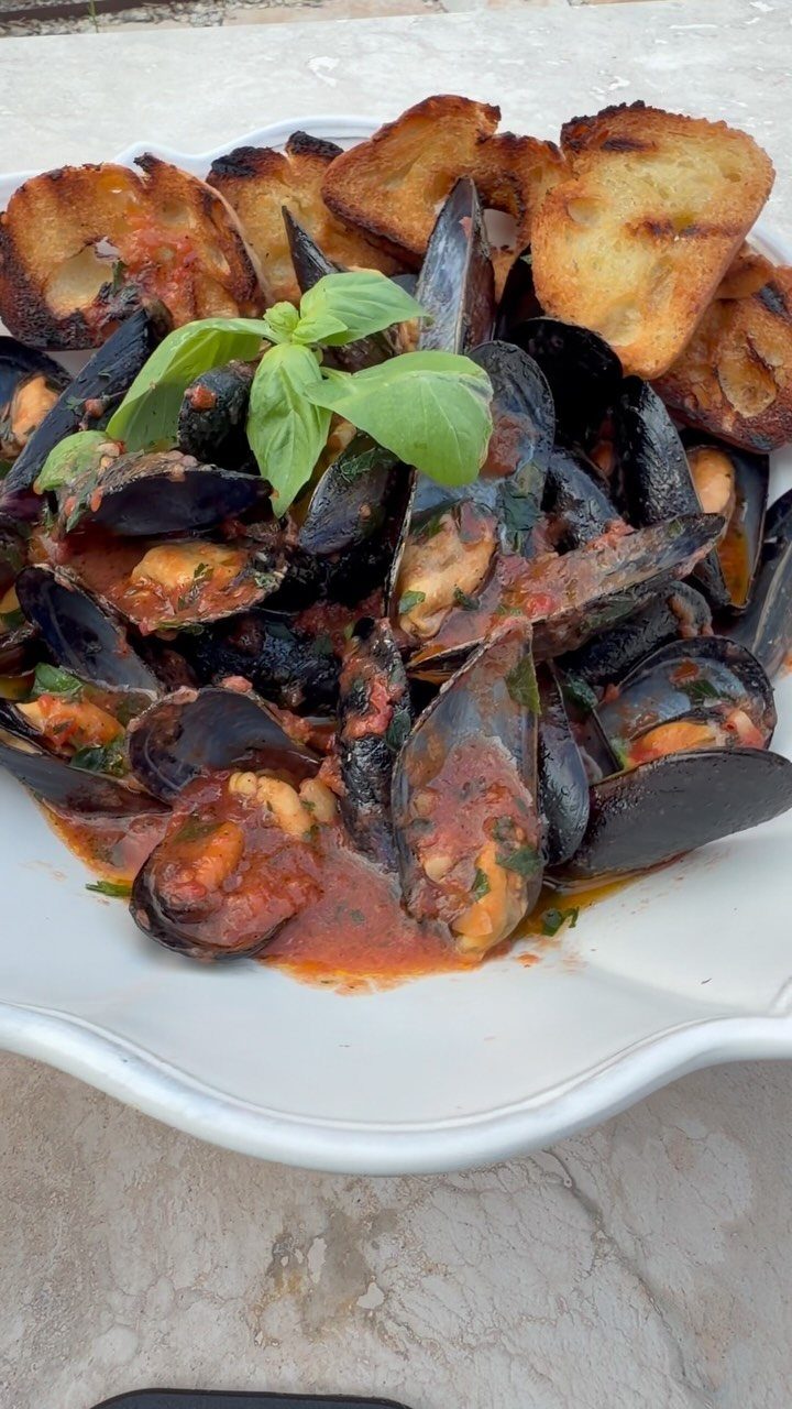 Mussels in red marinara sauce garnished with basil and served with toasted bread.