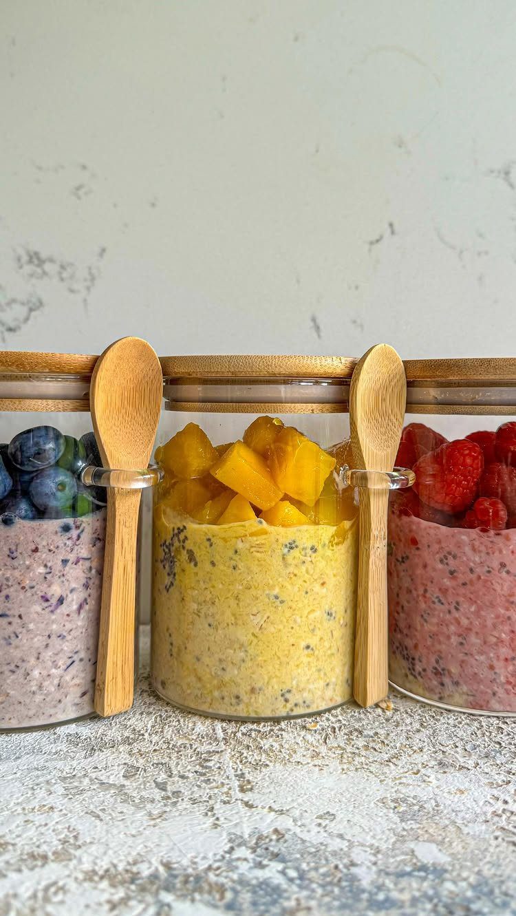 Three glass jars of overnight oats topped with blueberries, mango, and raspberries.