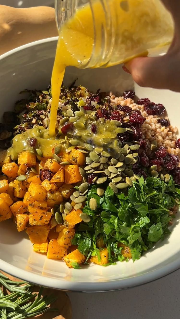 Roasted butternut squash bowl with seeds, cranberries, and grains being drizzled with dressing