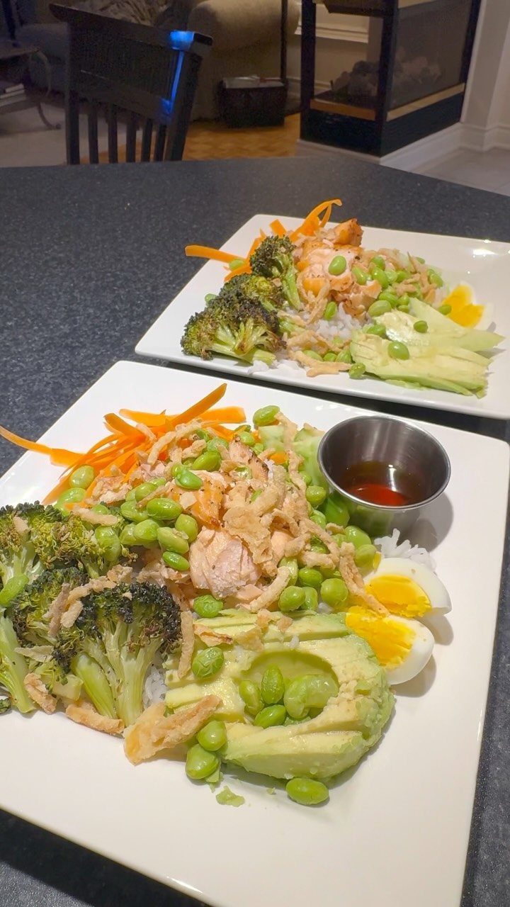 Salmon rice bowls with broccoli, avocado, edamame, and eggs on white square plates.