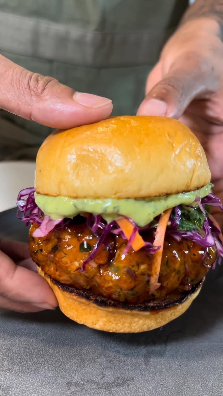 Salmon burger with purple cabbage slaw and green sauce in a brioche bun.