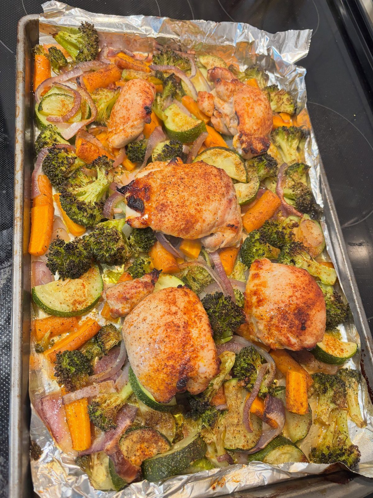 Roasted chicken thighs and mixed vegetables on a foil-lined baking sheet.