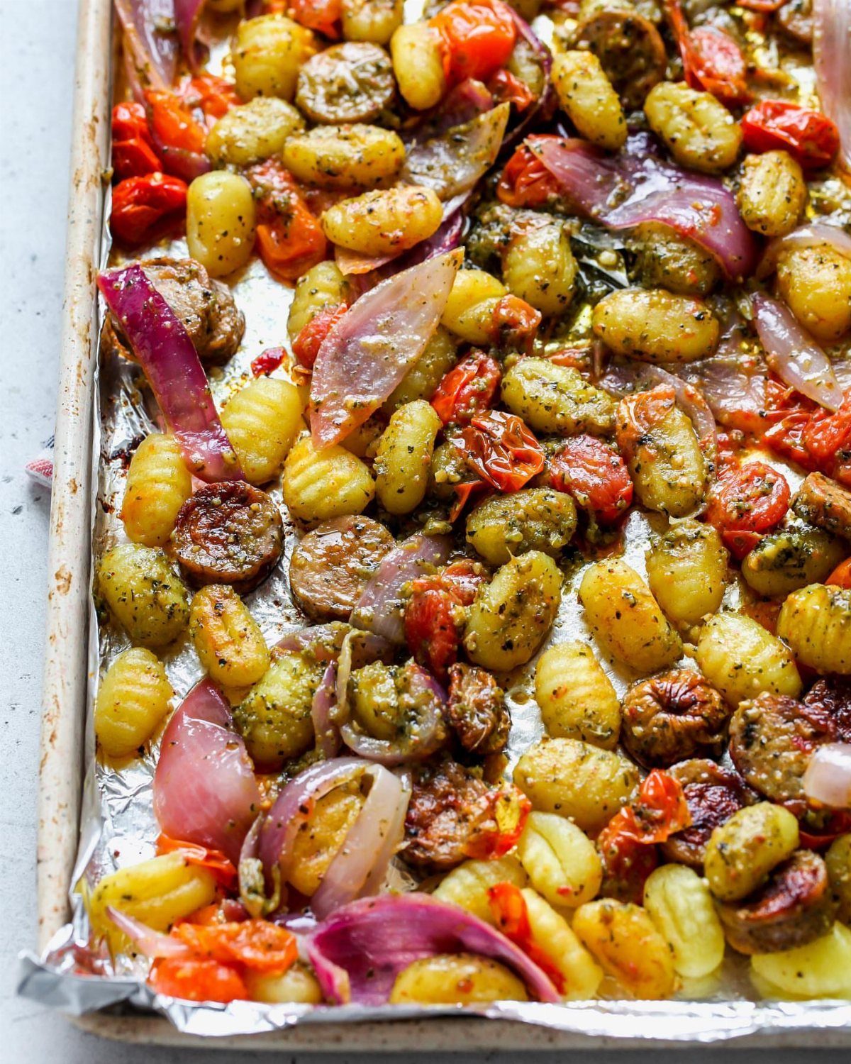 Roasted gnocchi with cherry tomatoes and red onions on a foil-lined baking sheet.