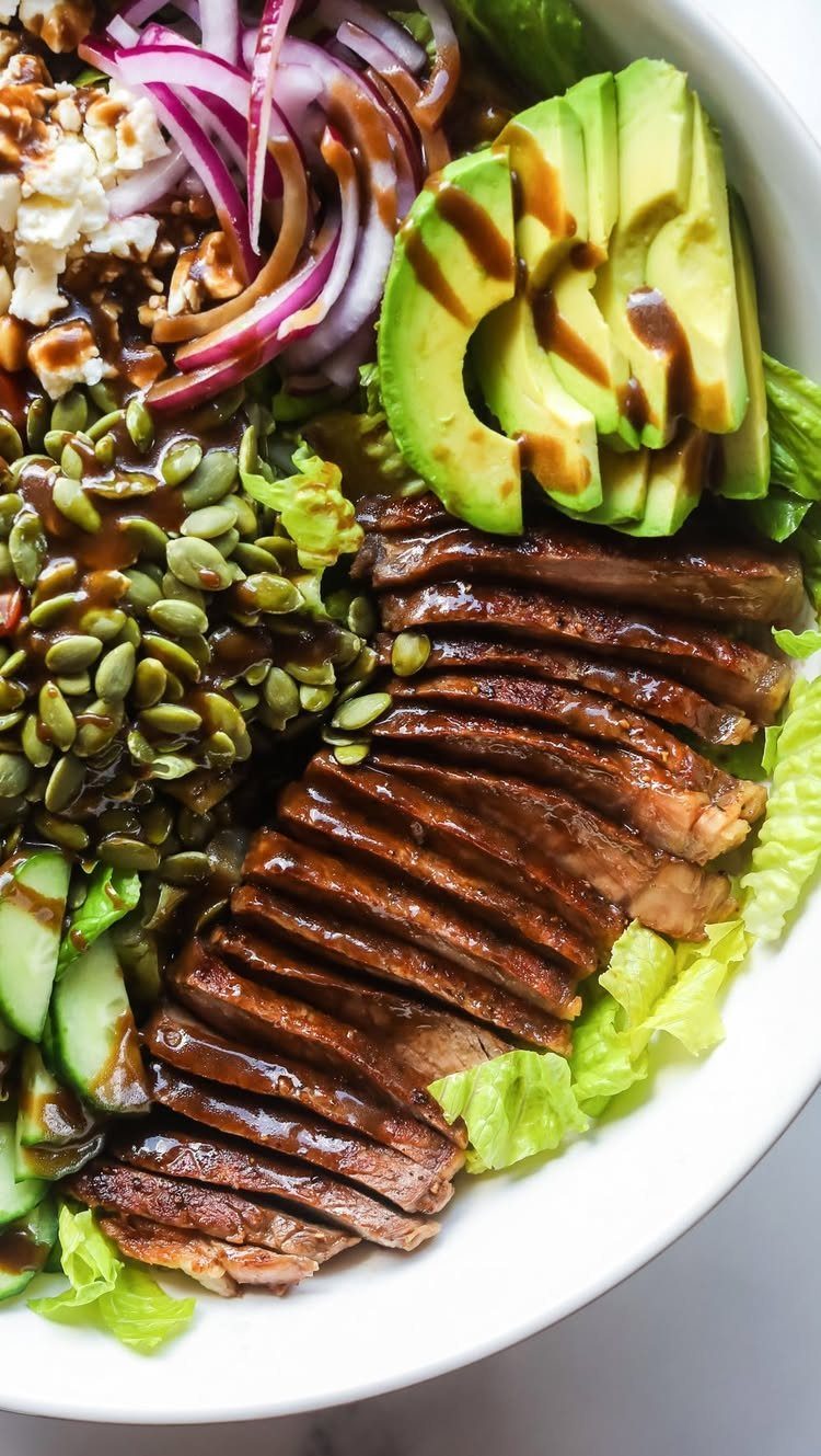Sliced grilled steak and avocado on a Greek salad with feta and seeds.