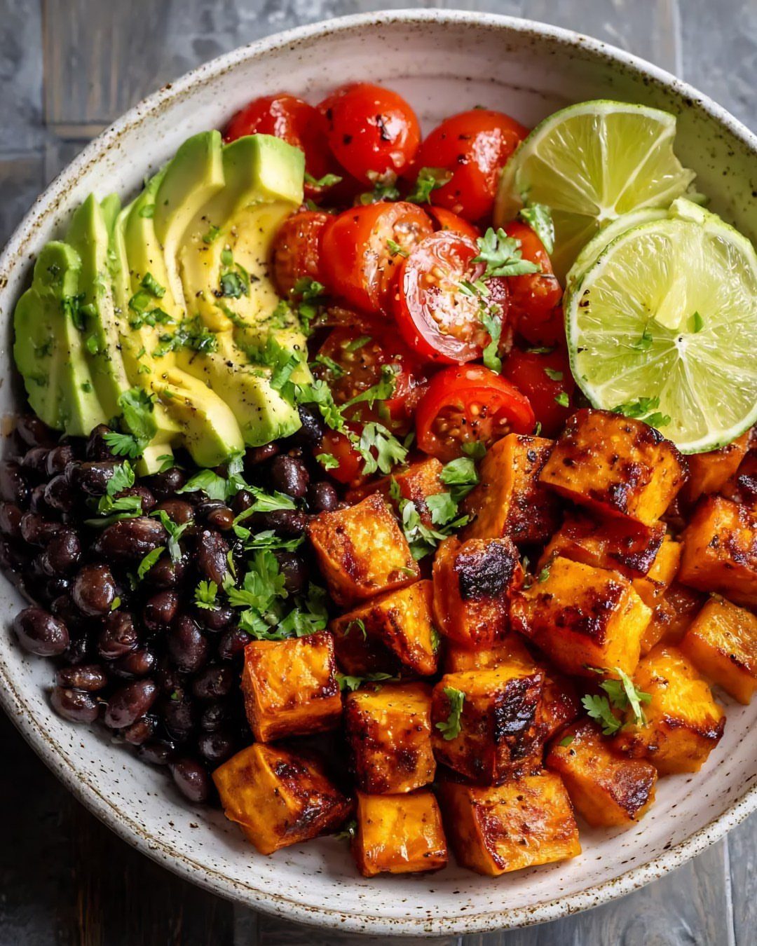 Sweet potato bowl with black beans, avocado, cherry tomatoes, and lime wedges.