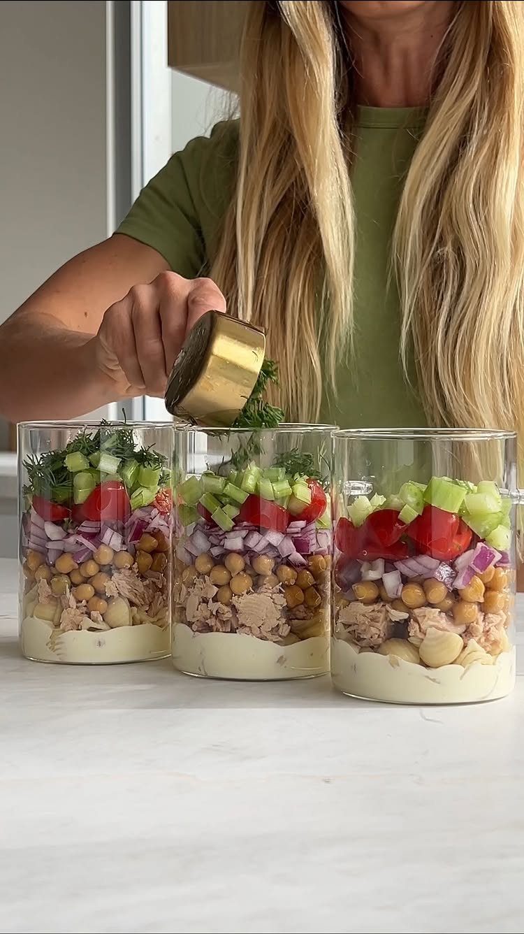 Three glass jars filled with layered tuna salad, chickpeas, and fresh vegetables.