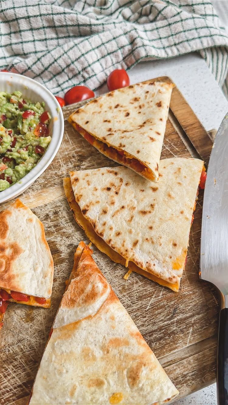 Toasted veggie quesadillas on a wooden board with a side of fresh guacamole.
