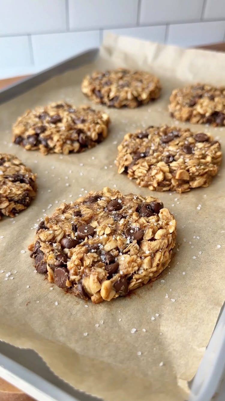26 Oats Recipes for Snacks, from Energy Bites to Oat Crackers 8 Oatmeal chocolate chip cookies on a parchment-lined baking sheet against white tiles.