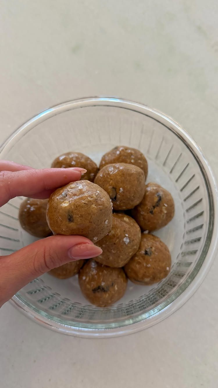 26 Oats Recipes for Snacks, from Energy Bites to Oat Crackers 15 Hand holding a brown cinnamon oatmeal bite over a bowl of oat balls.
