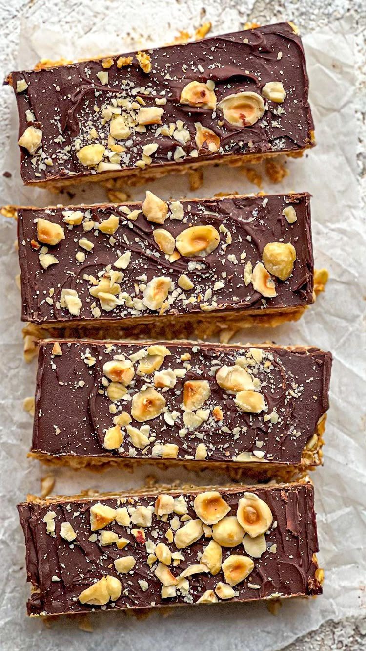 26 Oats Recipes for Snacks, from Energy Bites to Oat Crackers 4 Chocolate topped oat bars with chopped hazelnuts on white parchment paper