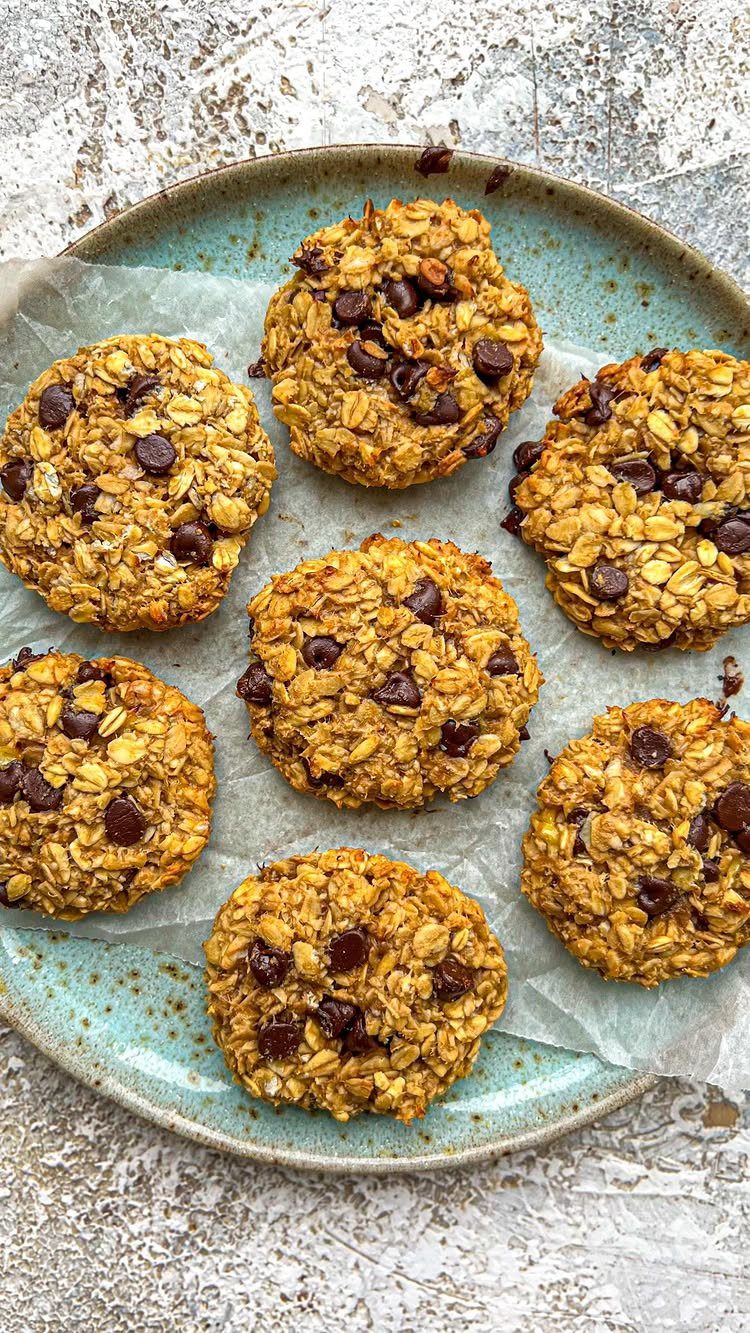 26 Oats Recipes for Snacks, from Energy Bites to Oat Crackers 13 Oatmeal cookies with chocolate chips on a blue plate with parchment paper.