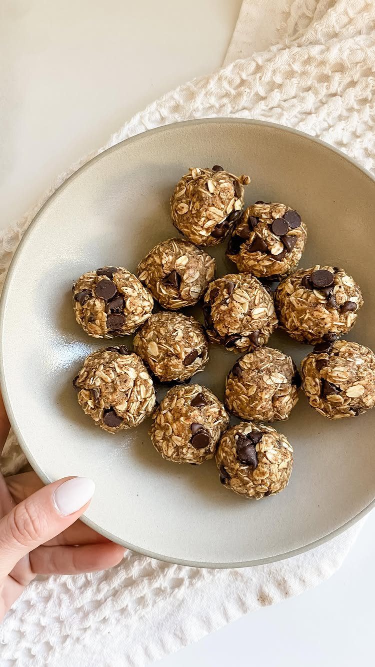 26 Oats Recipes for Snacks, from Energy Bites to Oat Crackers 2 Oatmeal energy bites with chocolate chips on a grey plate held by a hand.
