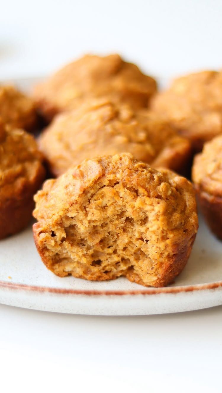 26 Oats Recipes for Snacks, from Energy Bites to Oat Crackers 7 Pumpkin oat muffins on a white plate with one muffin showing a bite mark.