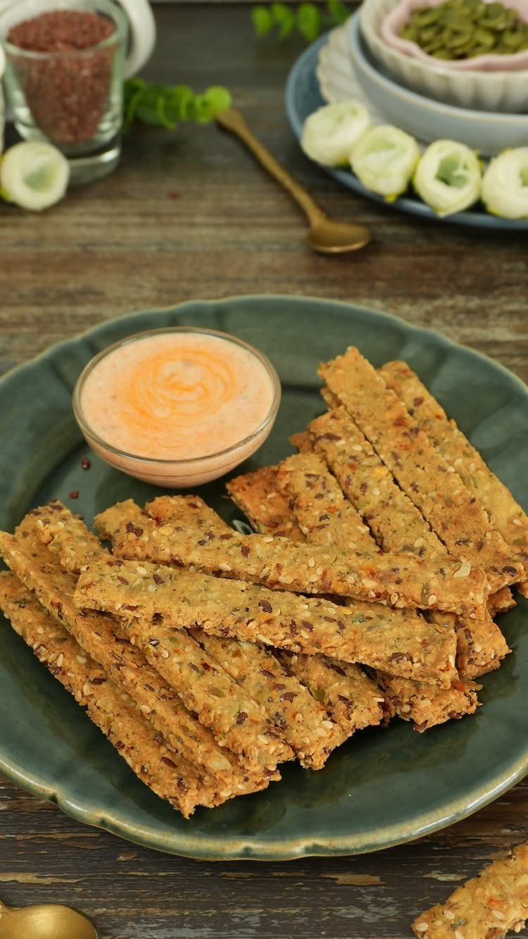 26 Oats Recipes for Snacks, from Energy Bites to Oat Crackers 16 Savory oat crackers with seeds on a green plate with orange dipping sauce.