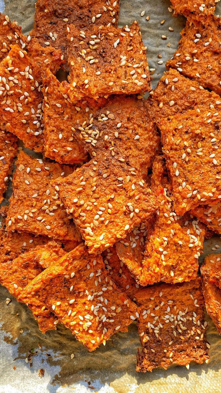 26 Oats Recipes for Snacks, from Energy Bites to Oat Crackers 23 Savory orange-brown oat crackers topped with white sesame seeds on parchment paper.