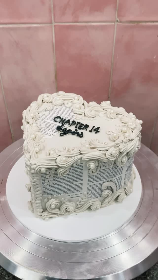 13 Open Book Cakes, from Fairytale Pages to Library Shelves 10 Heart-shaped open book cake with white frosting swirls and printed text on top.
