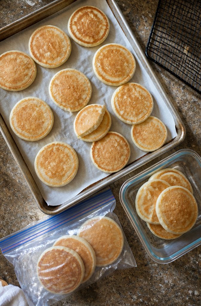 Easy Pancake Recipe with Self-Rising Flour for Fluffy Stacks 10 Pancakes cooling on a baking sheet beside a freezer bag