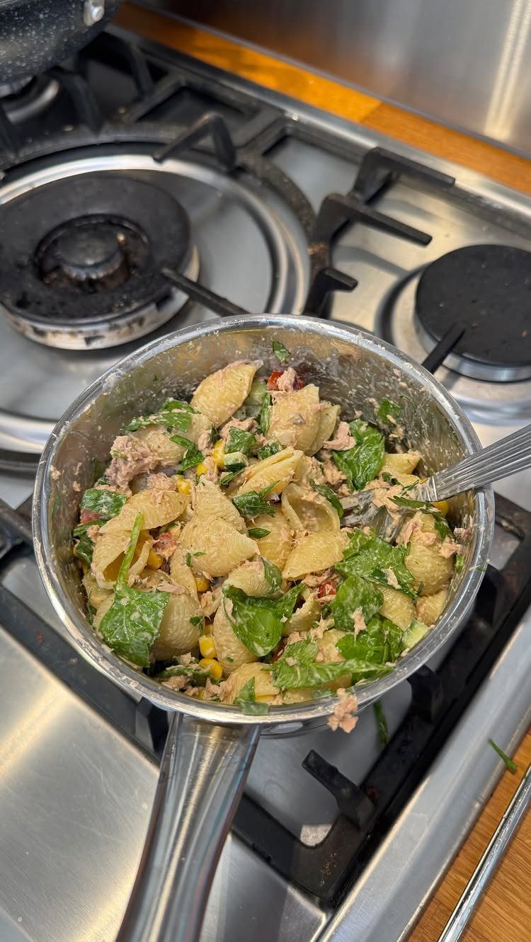 Shell pasta with tuna, corn, and spinach in a stainless steel pan.