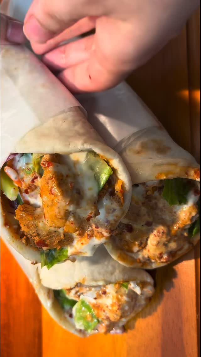 Chicken shawarma wraps with seasoned meat and vegetables wrapped in white paper.