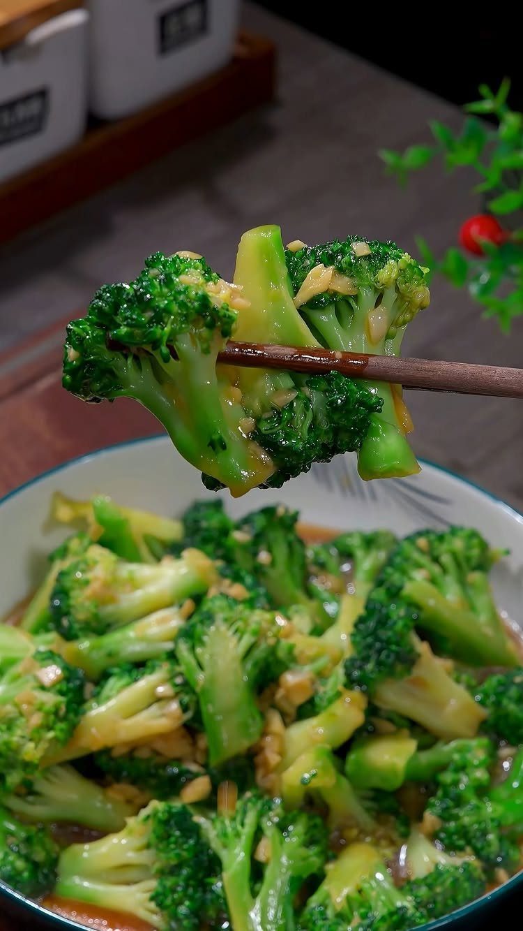 Sautéed broccoli with garlic held by chopsticks over a bowl of vegetables