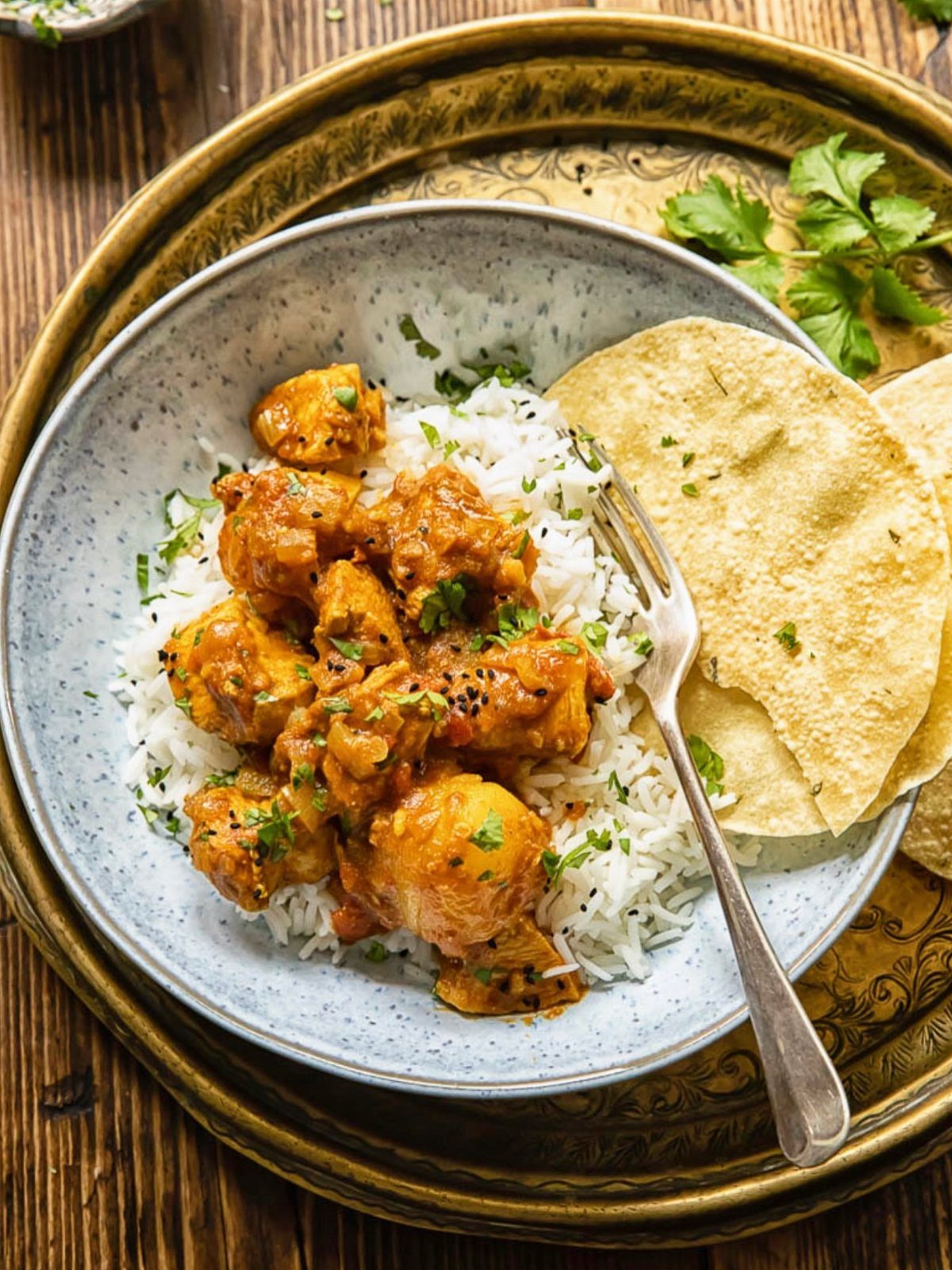 Chicken curry with white rice and papadum served in a bowl on a gold platter.