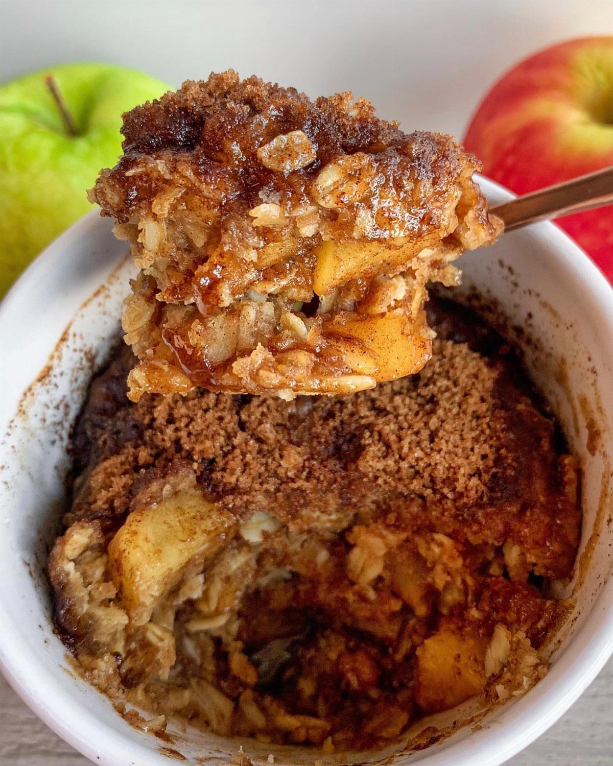 Apple crumble with oats and cinnamon in a white bowl with fresh apples.