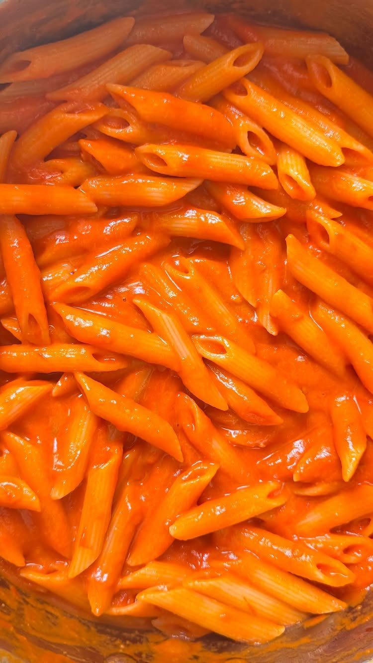 Penne pasta mixed with a rich red tomato sauce inside a cooking pot.