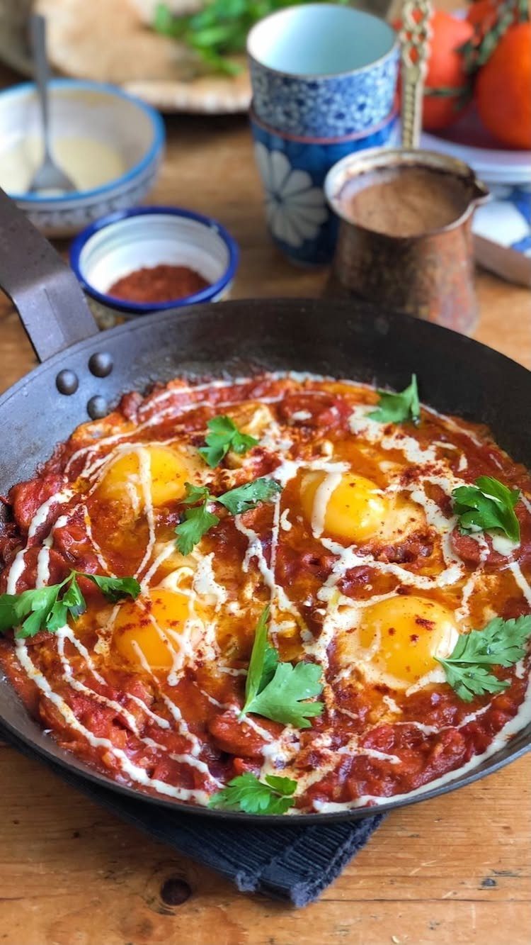 Shakshuka with poached eggs in a black skillet, garnished with cream and parsley.