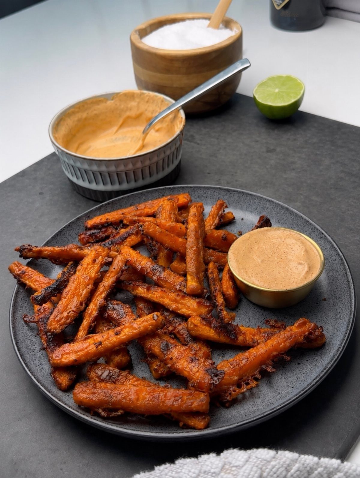 Roasted carrot fries on a black plate with a side of dipping sauce.