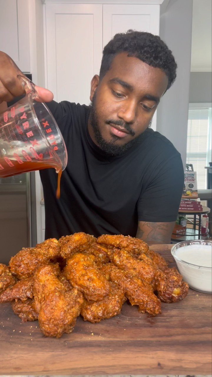 Man pouring honey glaze over a large pile of fried chicken wings.
