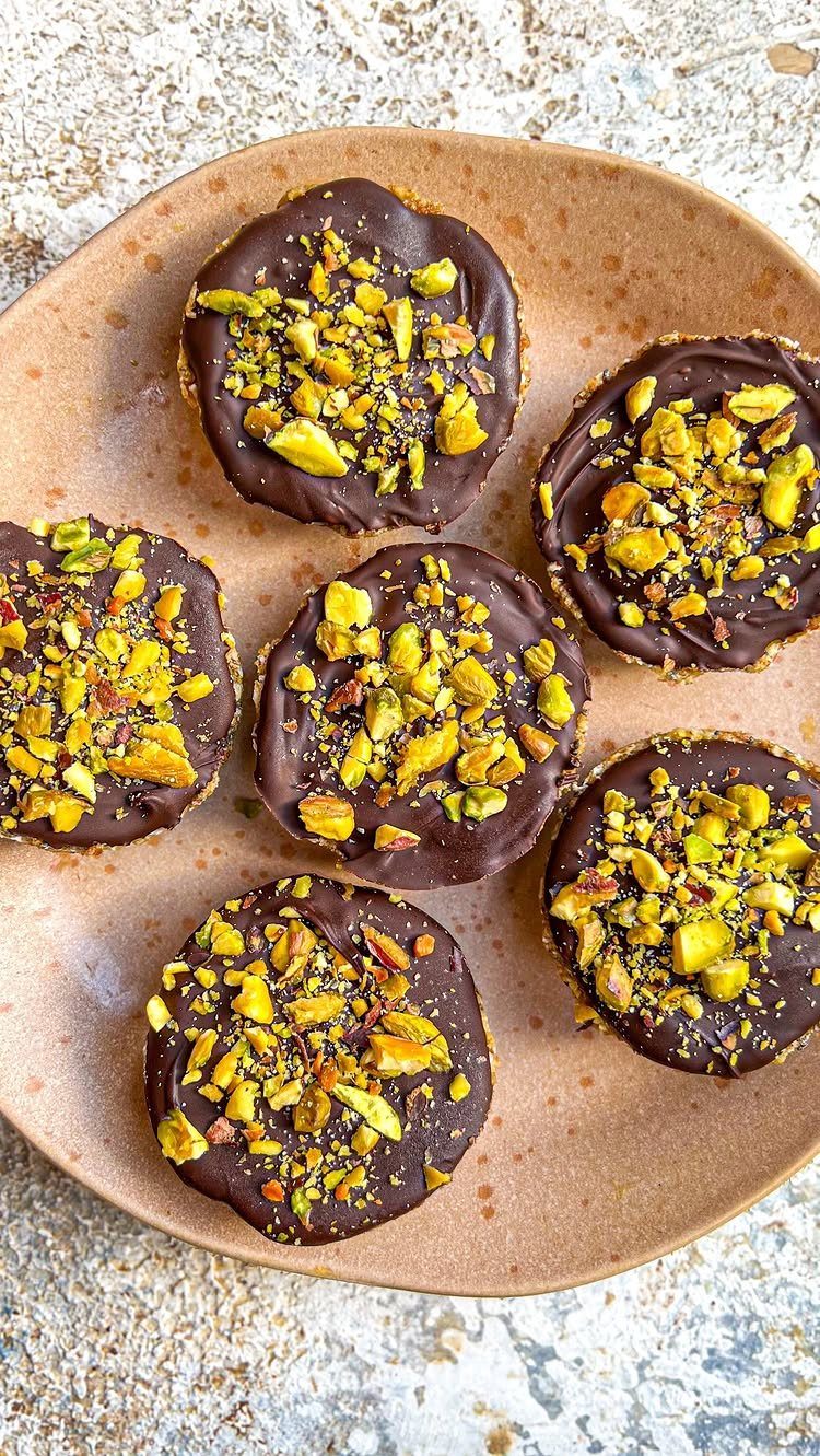 Chocolate tarts topped with crushed pistachios on a brown ceramic plate.