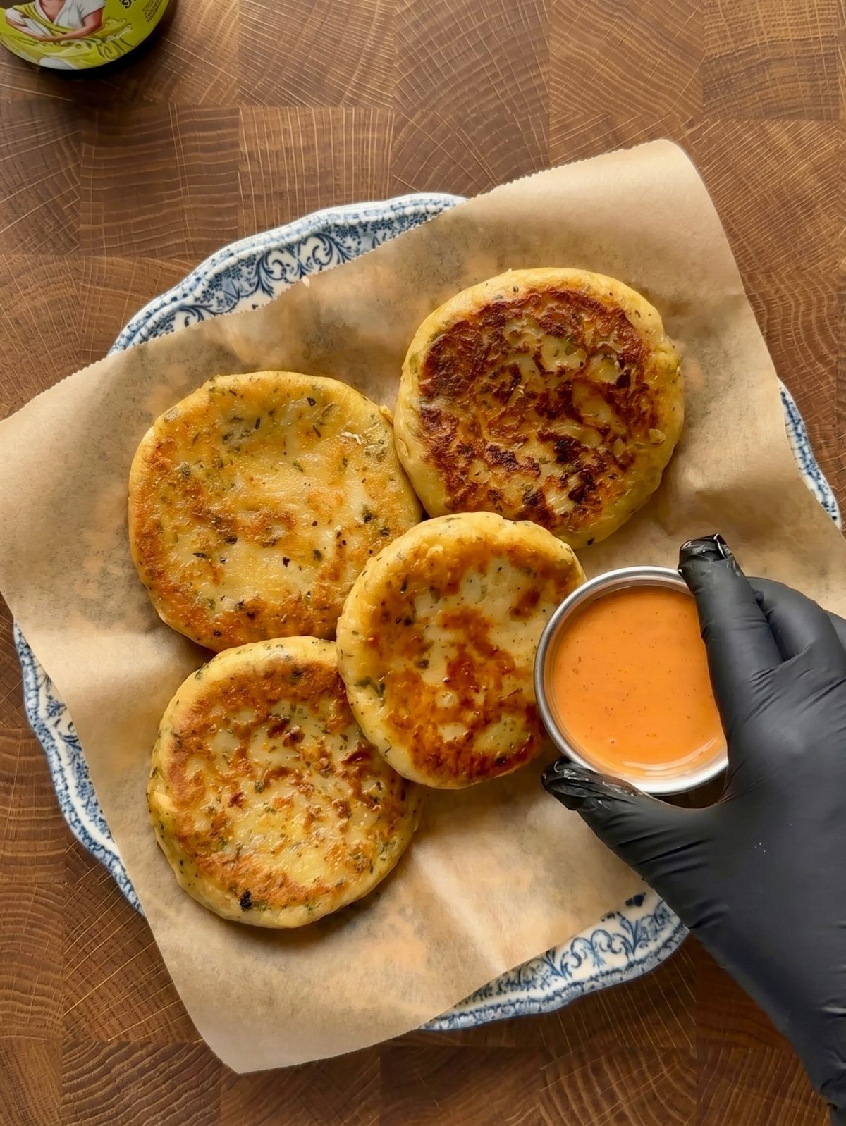 Four golden-brown potato cakes on parchment paper with a side of orange dipping sauce.