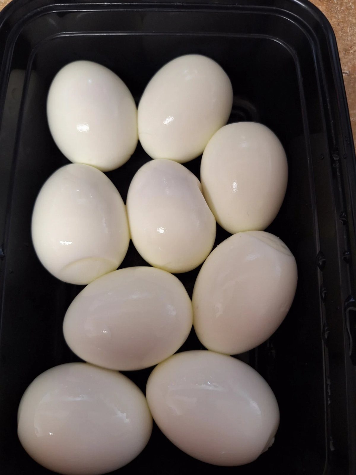 Peeled hard-boiled eggs arranged in a black plastic storage container.