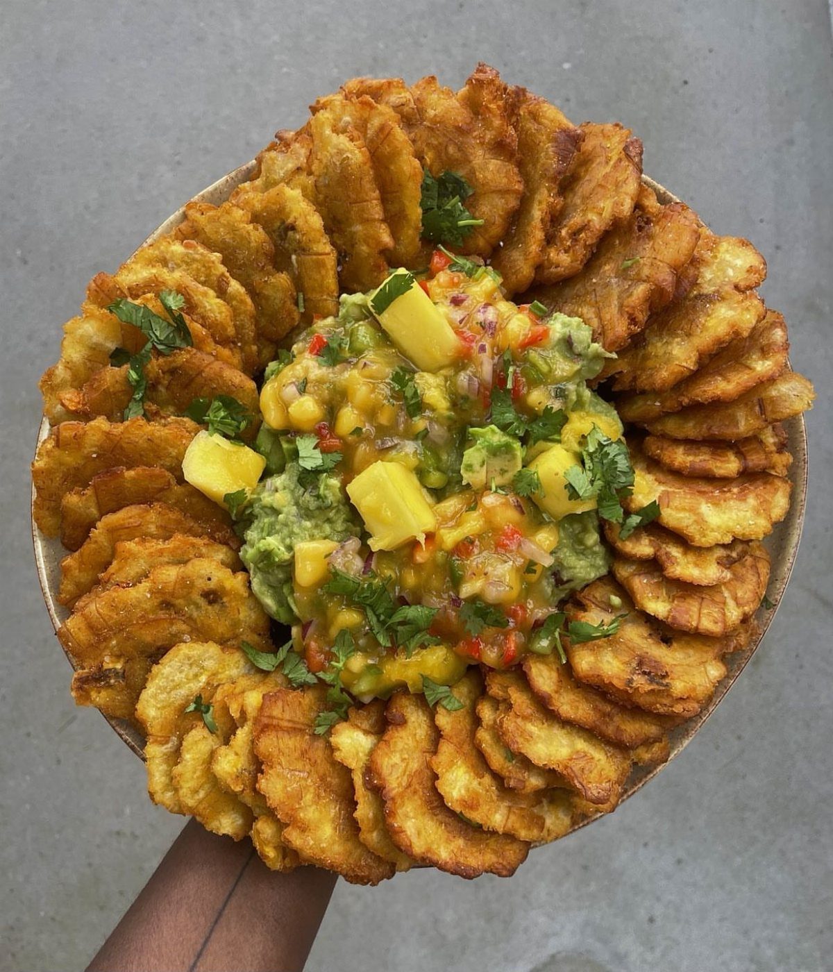 Guacamole with corn and mango surrounded by fried plantain chips on a plate.