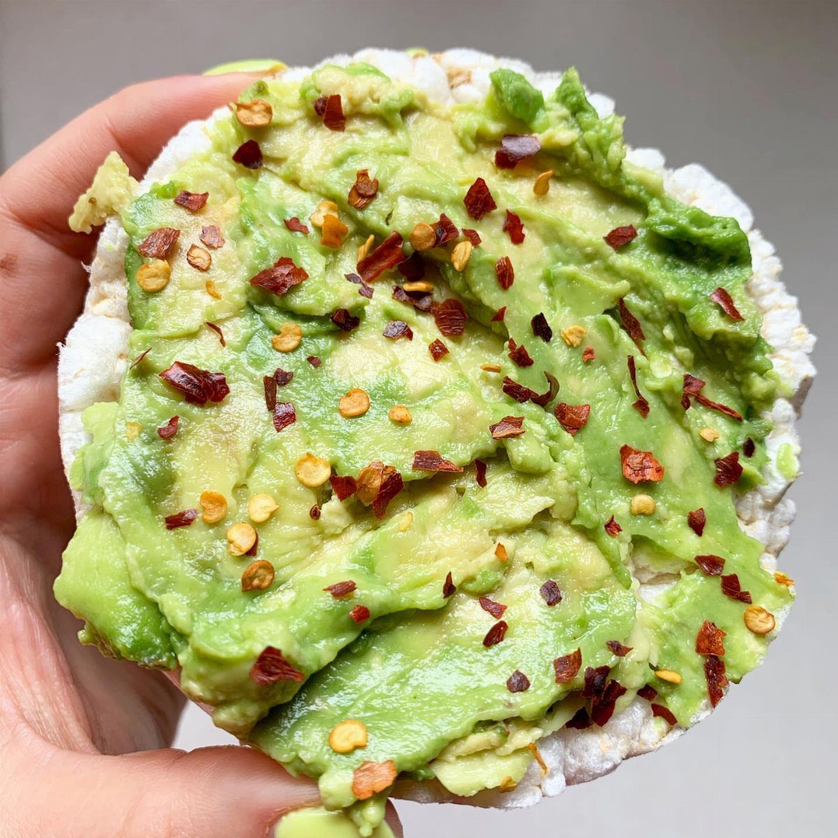 Rice cake topped with mashed avocado and red chili flakes held in a hand