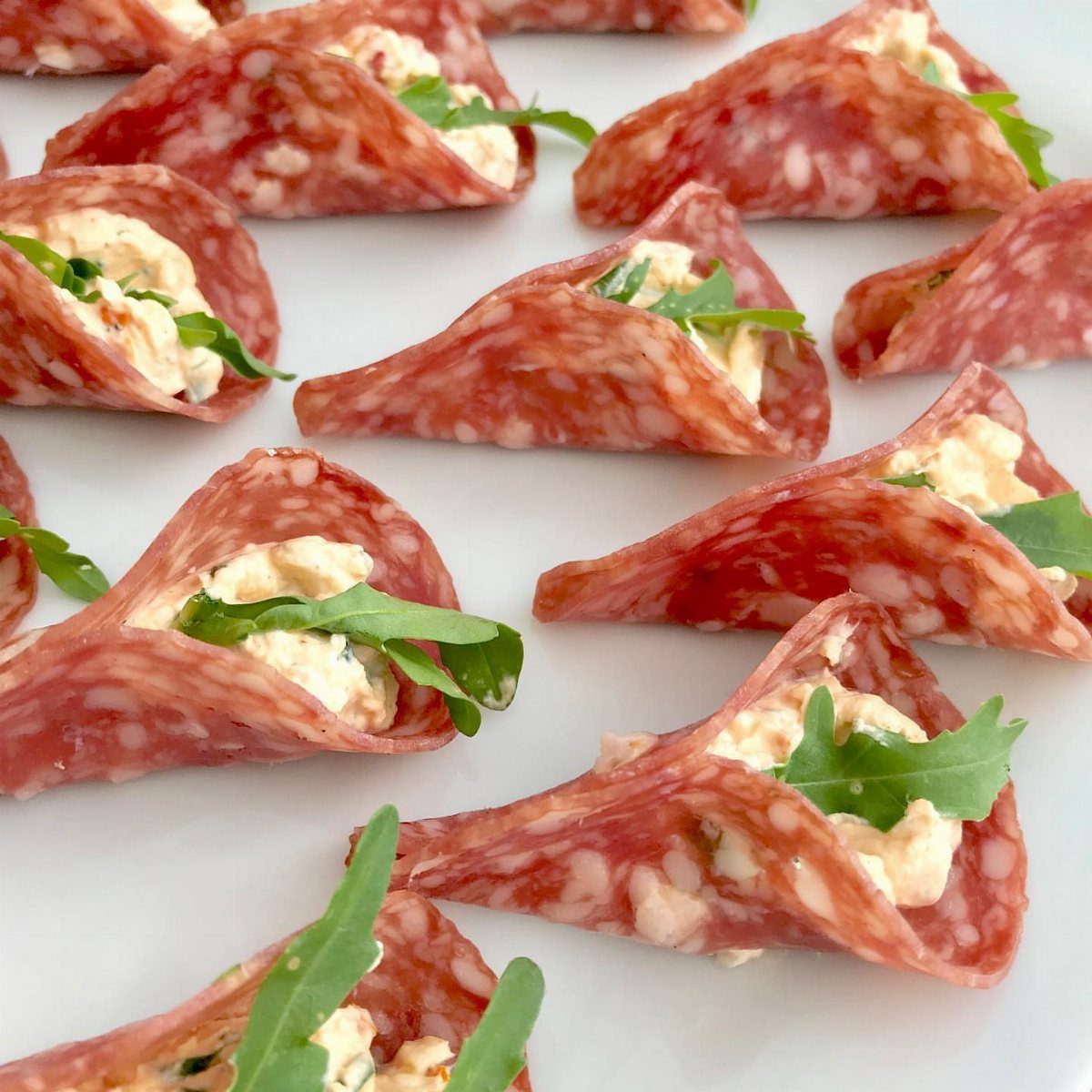 Salami slices folded into cones filled with cream cheese and fresh arugula leaves.