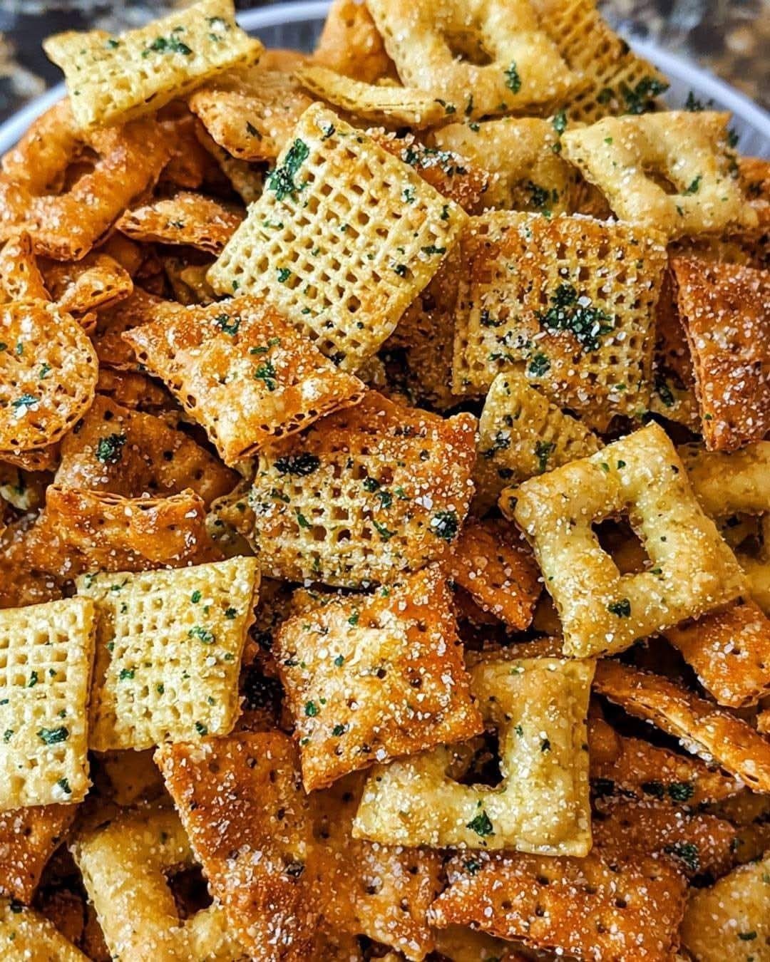 Seasoned cracker snack mix with herbs and seeds in a white bowl