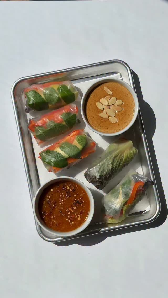 Vietnamese rice paper rolls with peanut and chili dipping sauces on a metal tray.