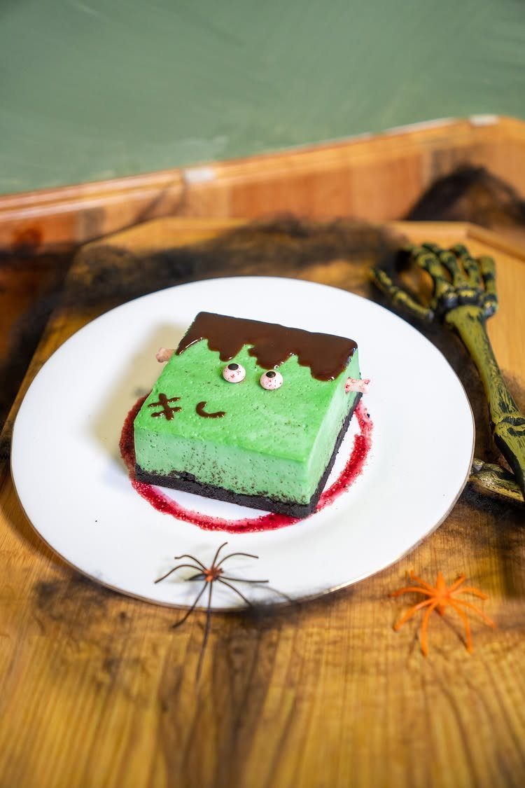 Green Frankenstein monster cake slice with candy eyes on a white plate.