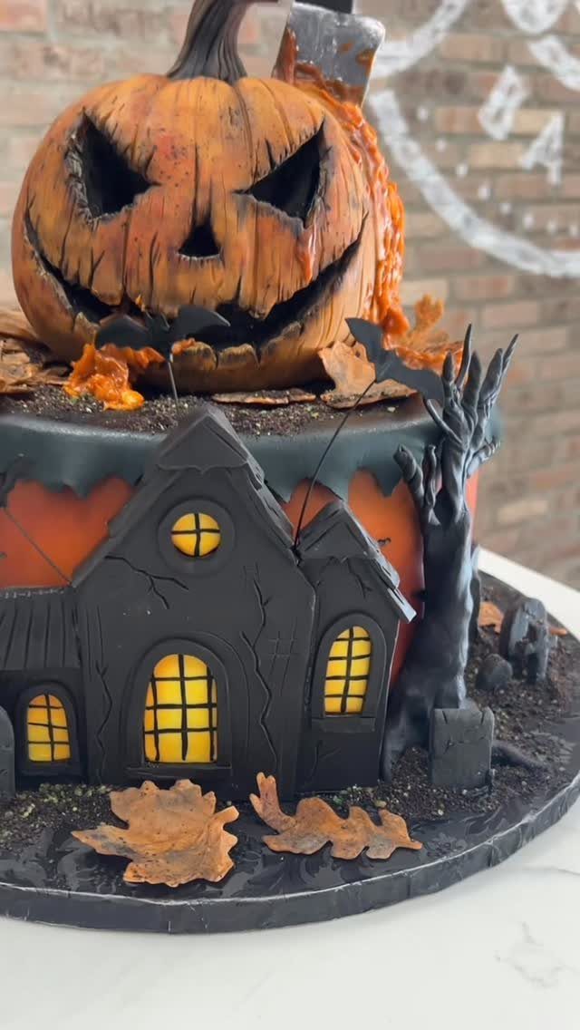 Spooky Halloween cake with a carved pumpkin and a haunted house with glowing windows.