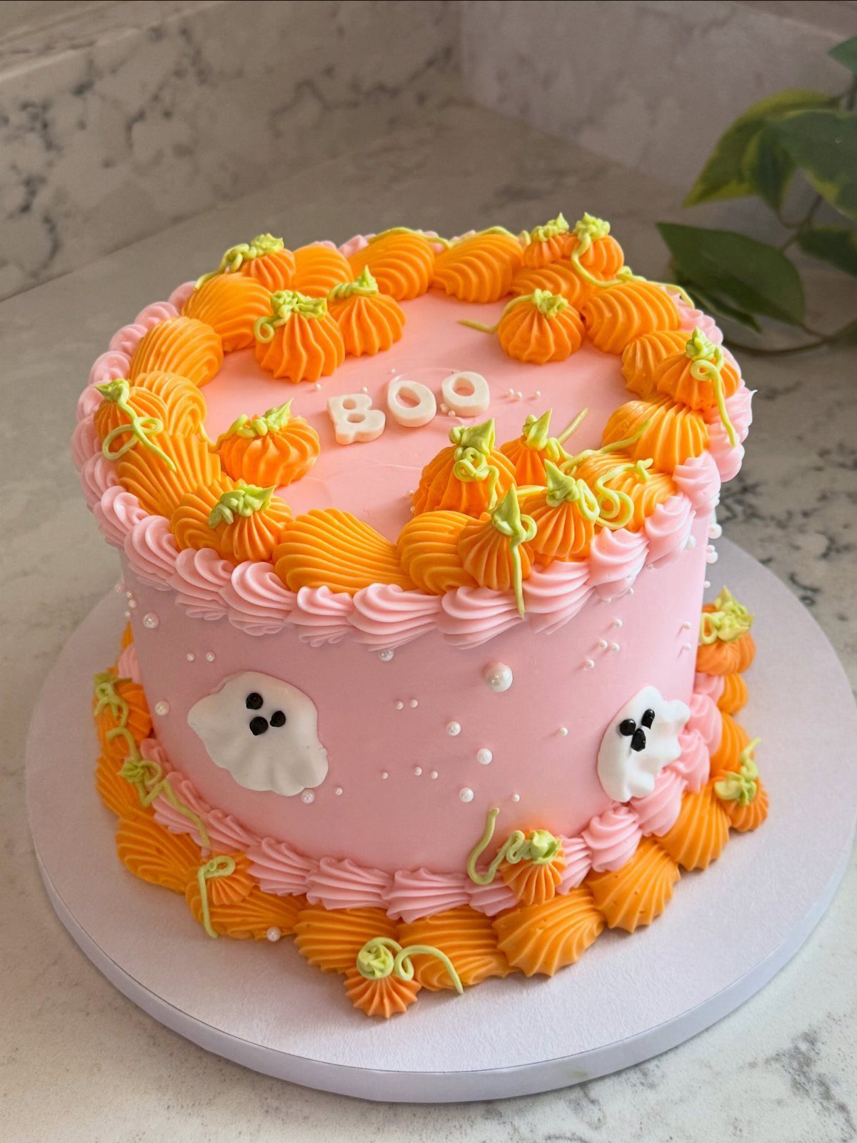 Pink Halloween cake with orange pumpkin frosting, white ghosts, and a BOO topper.