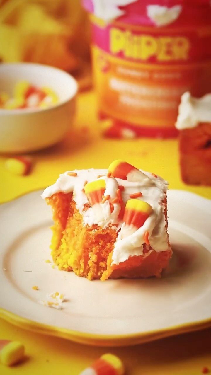 Orange cake slice with white frosting and candy corn on a white plate.
