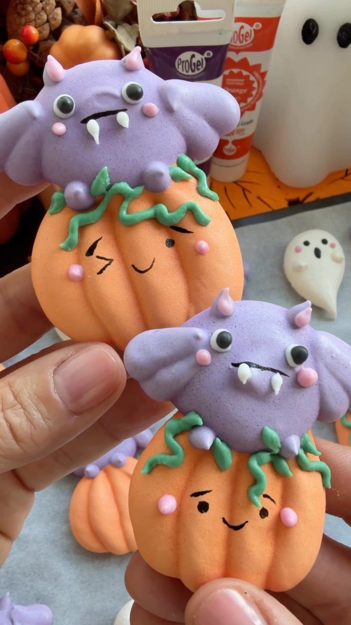 Small pumpkin cakes topped with purple bats held in a person's hands.