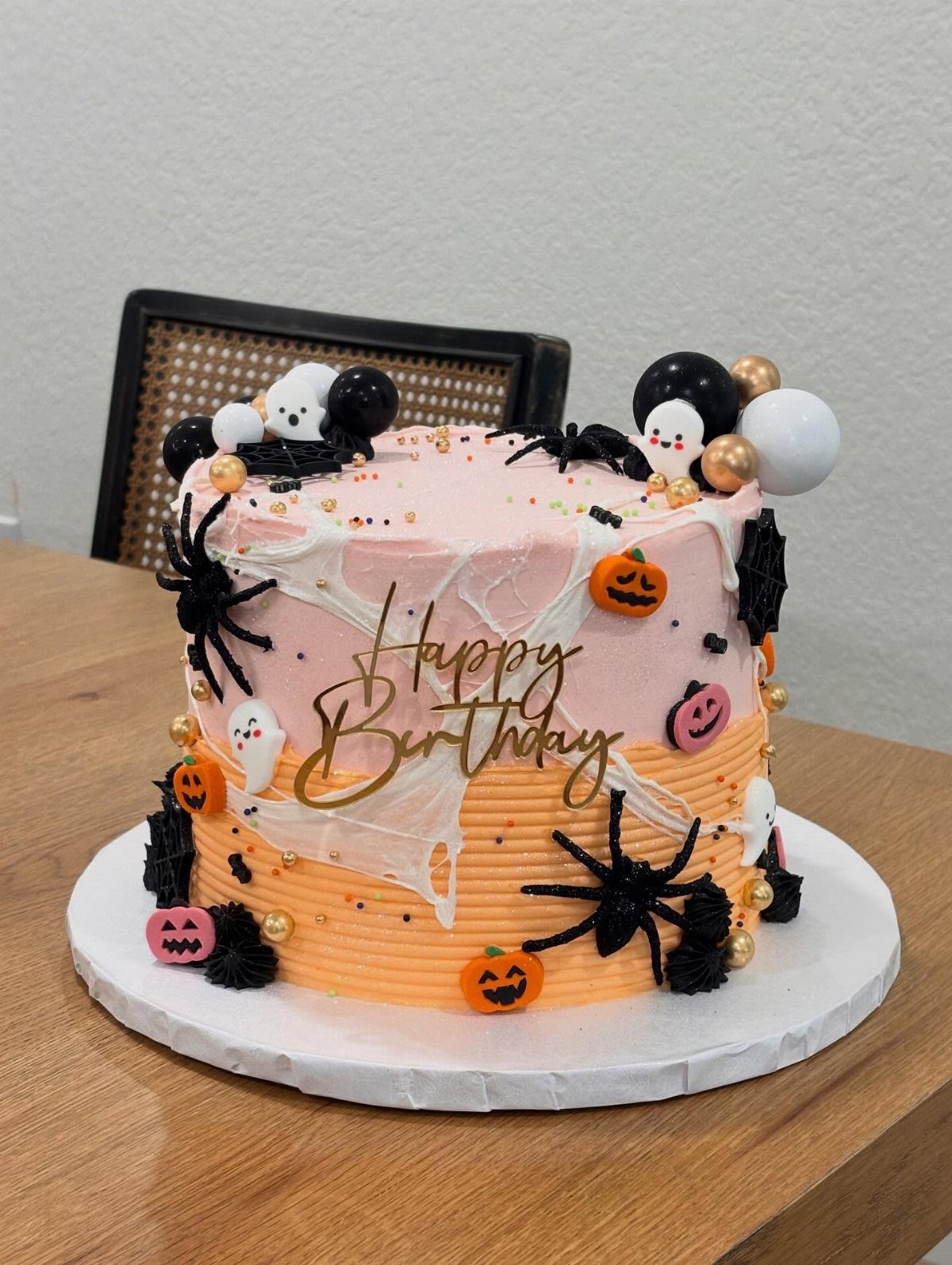 Halloween birthday cake with pink and orange frosting decorated with black spiders and pumpkins.
