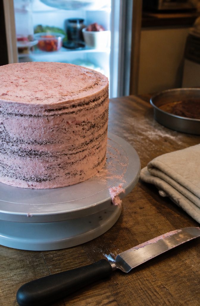 Stacked chocolate cake with strawberry jam and a thin patchy buttercream coat